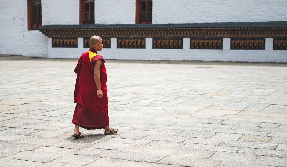 A Buddhist monk in traditional attire walks through a courtyard in Bhutan, showcasing spiritual tranquility.