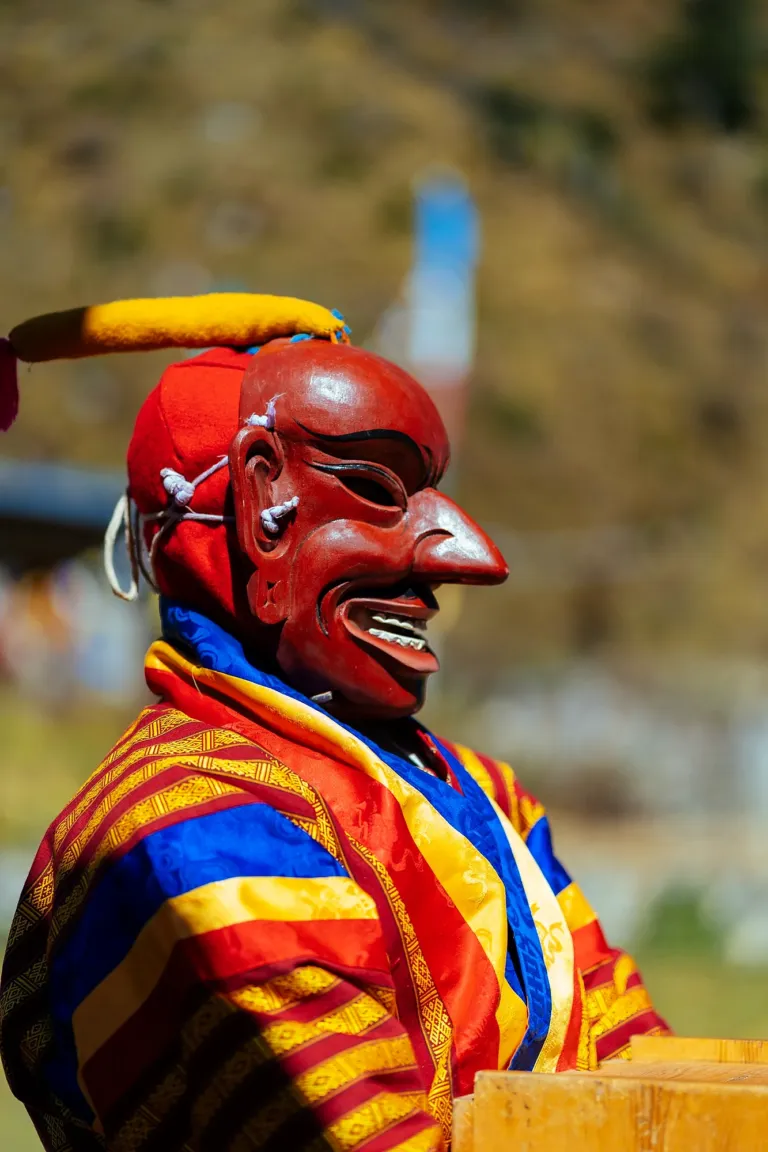 An atsara, the masked jester of Bhutanese festivals, in a red mask and bright robes