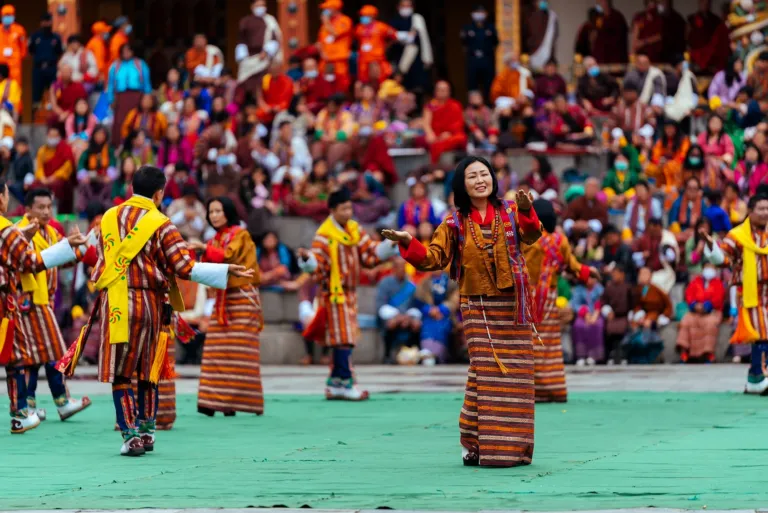 Folk dancers in gho and kira performing before crowds in a dzong courtyard during a festival
