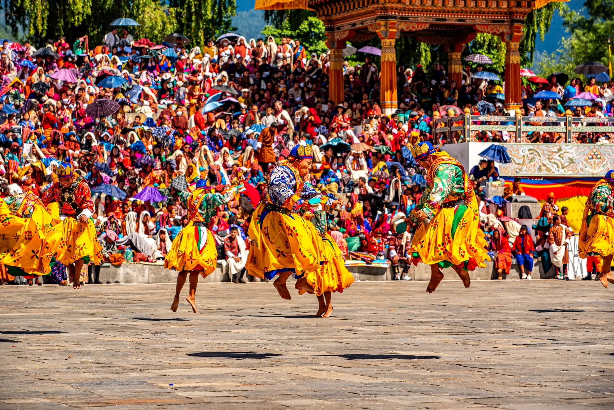 Masked dancers in yellow skirts leaping during a cham dance before a festival crowd